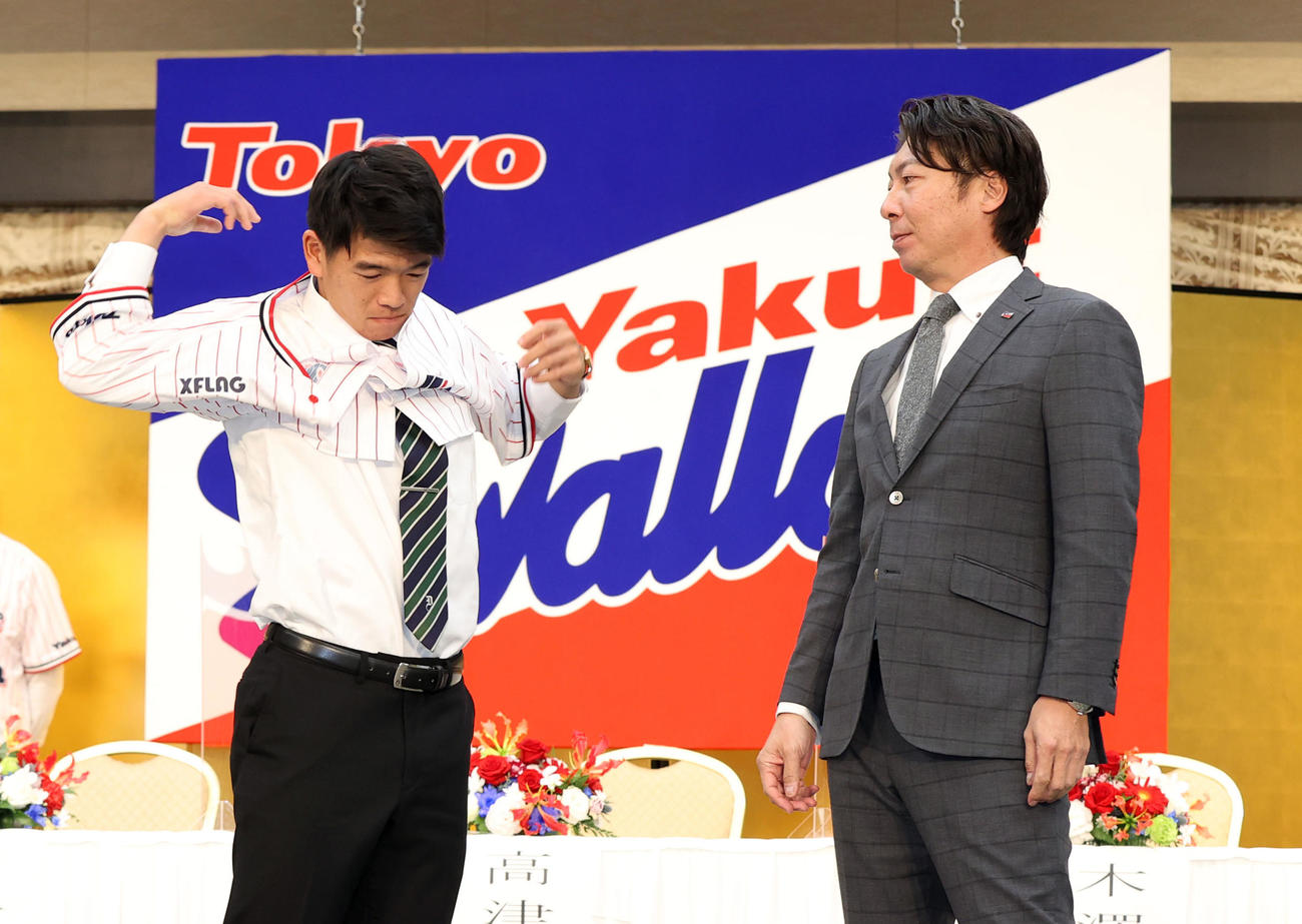 ヤクルト新入団発表会見で高津監督（右）からユニホームを着せてもらうドラフト5位の獨協大・並木（撮影・狩俣裕三）