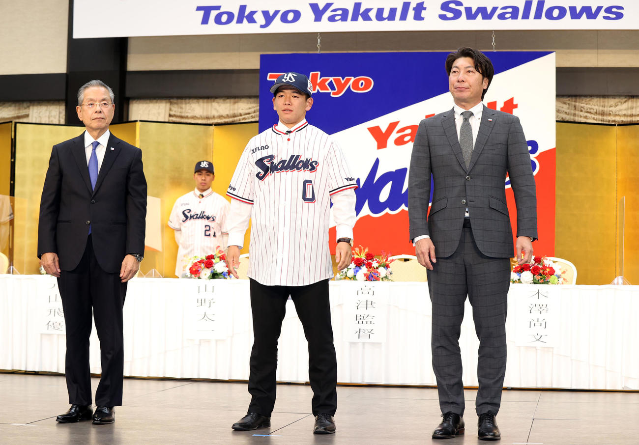 ヤクルト新入団発表会見で高津監督（右）からユニホームを着せてもらった後、記念撮影するドラフト5位の独協大・並木（中央）。左は衣笠球団社長（撮影・狩俣裕三）