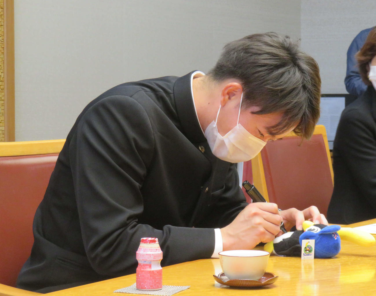ヤクルトのドラフト1位、慶大・木沢は千葉・船橋市役所を表敬訪問し、つば九郎のぬいぐるみの小ささに苦戦しながらサインを書き込む