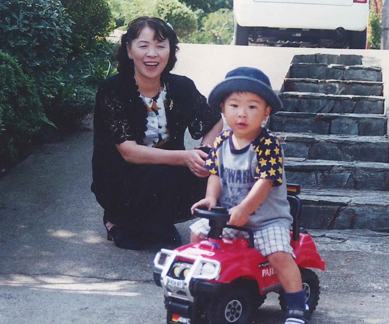 宮城・村田町へ夏の帰省時、祖母美智恵さん（左）の前でオモチャの車に乗る佐藤輝明（佐藤勲さん提供）