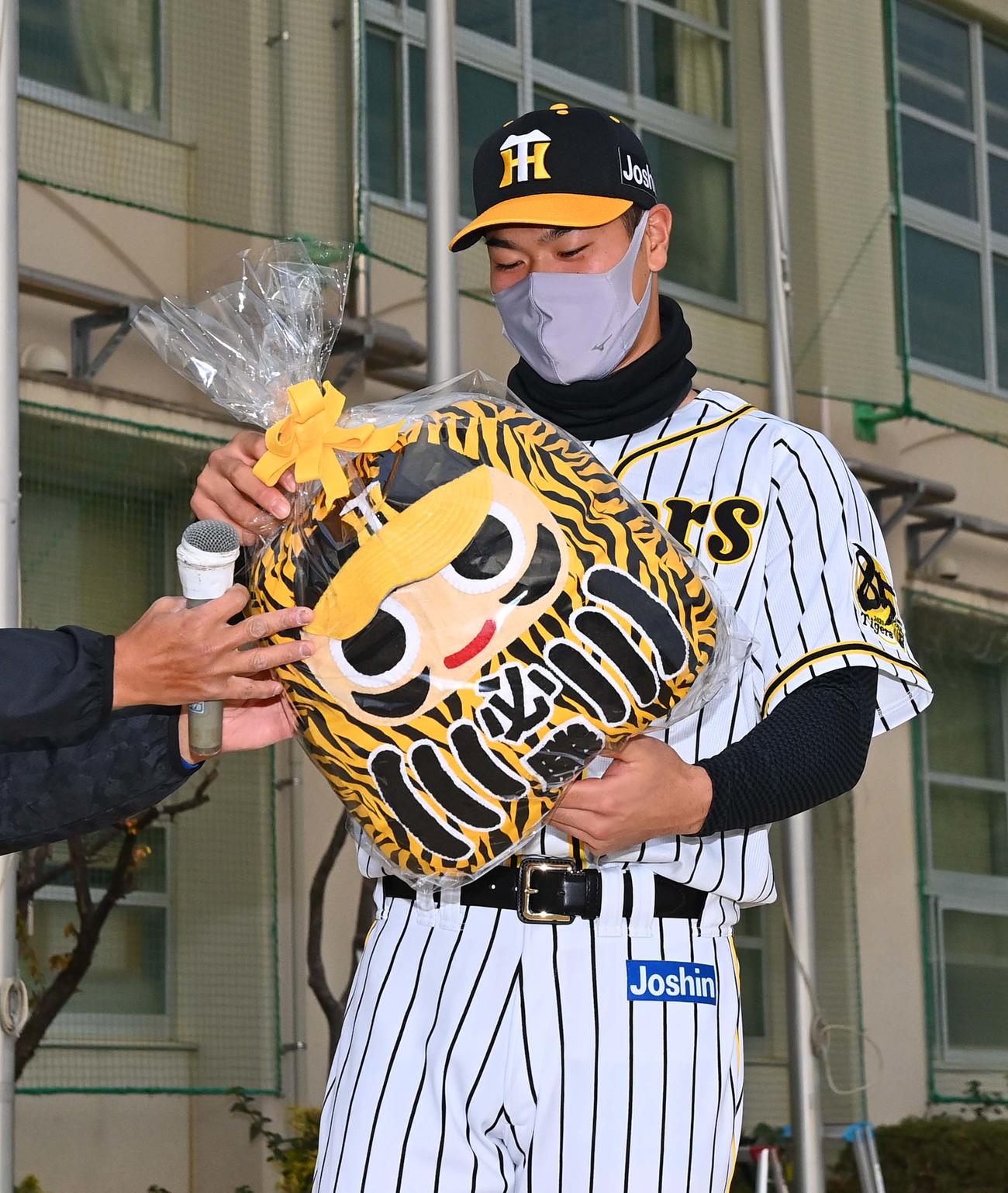 小学校時代に所属した甲東ブルーサンダースから贈られた必勝ダルマクッションを手に笑顔を見せる阪神佐藤輝（撮影・上田博志）