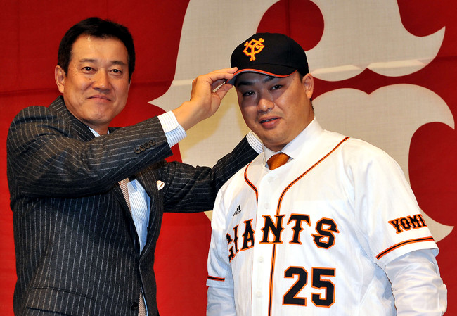 2011年12月13日、巨人入団会見で村田修一（右）は、笑顔の原辰徳監督に帽子をかぶせてもらう