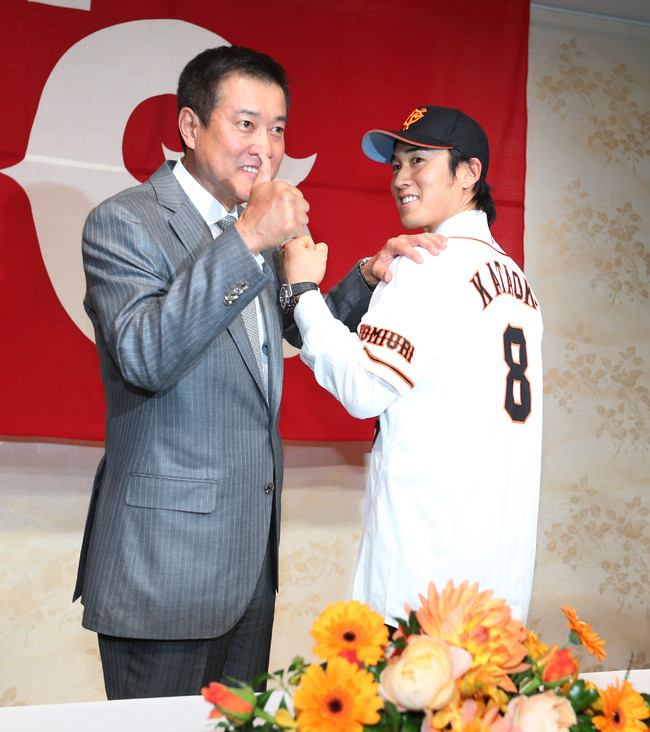 2013年12月9日、巨人への入団会見で、背番号8のユニホームを着てガッツポーズを見せる片岡治大（右）と、背中を見つめる原辰徳監督