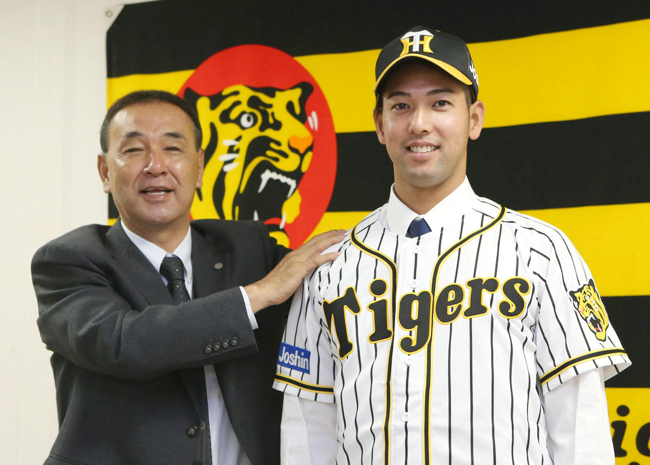 入団会見で木戸プロスカウト部長（左）から帽子をかぶせてもらう加治屋（代表撮影）