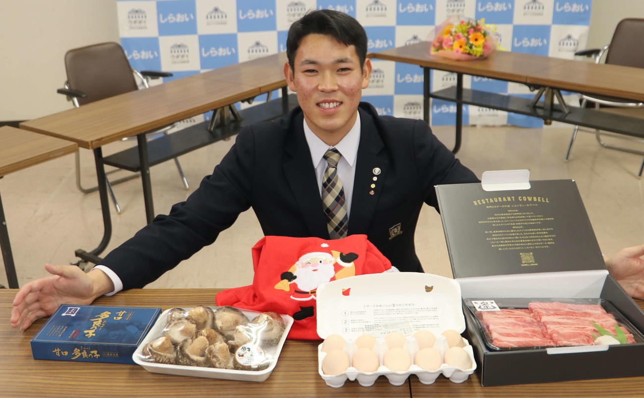 北海道日本ハムファイターズしらおい後援会より贈呈された白老町の特産品を前に笑顔をみせる日本ハムドラフト5位の根本（撮影・山崎純一）