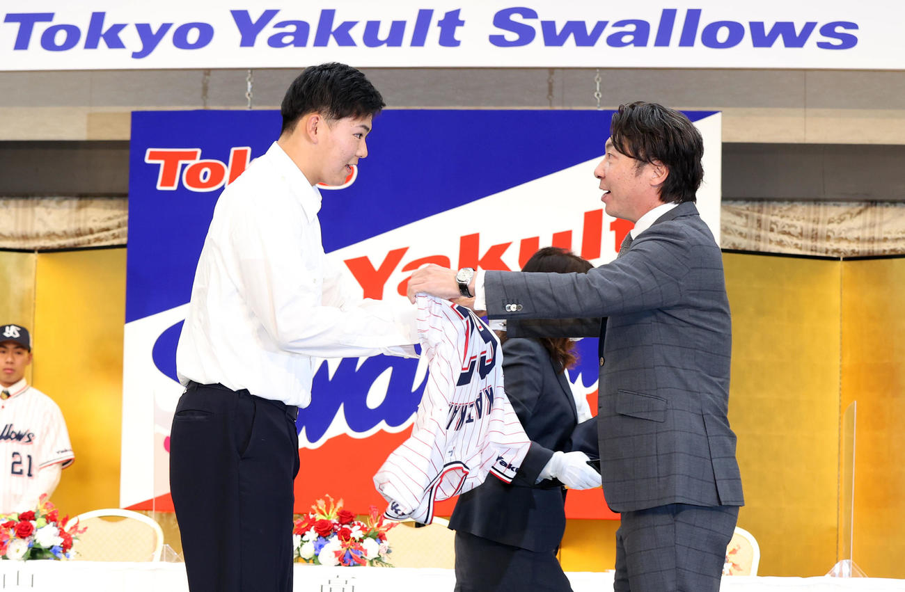 ヤクルト新入団発表会見で高津監督（右）からユニホームを着させてもらう嘉手苅（2020年12月1日撮影）