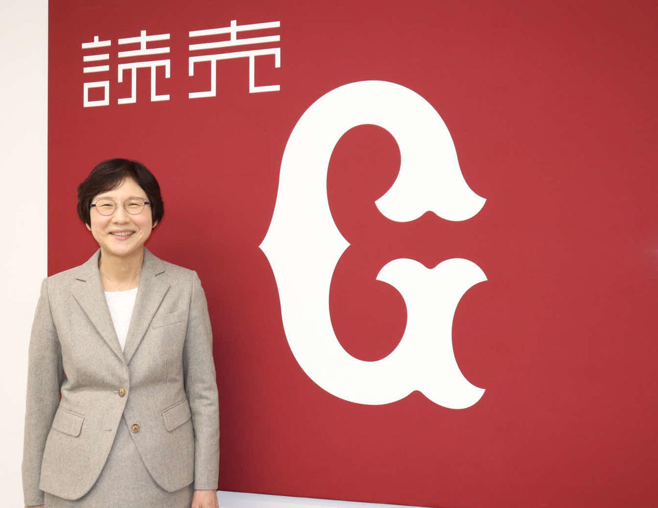 球団旗の前で笑顔を見せる巨人の場内放送係の山中さん（撮影・久永壮真）