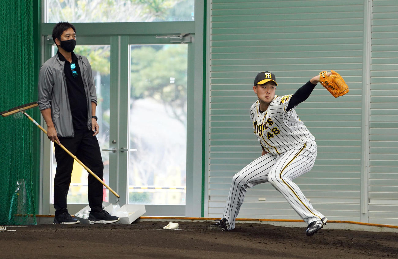 ブルペンで藤川SA（左）の指導を受けながら投球する阪神斎藤