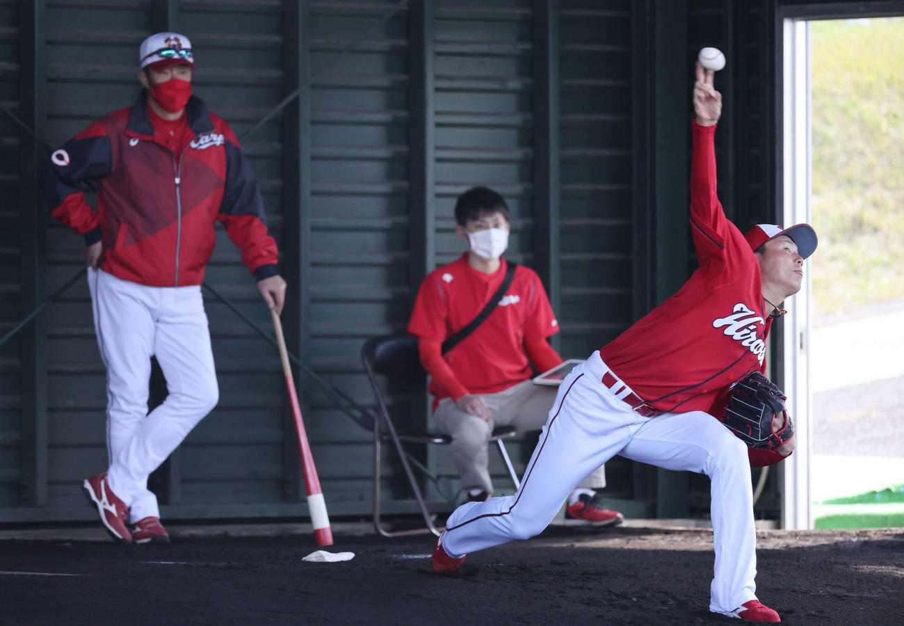 プロ野球広島沖縄キャンプ　ブルペンで投げるドラフト1位の栗林。左は佐々岡監督（撮影・加藤孝規）