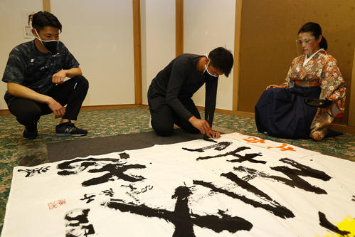 キャンプ休日に書道で今年の目標を書にしたためる中川颯（左）と山下。右は今井美恵子講師