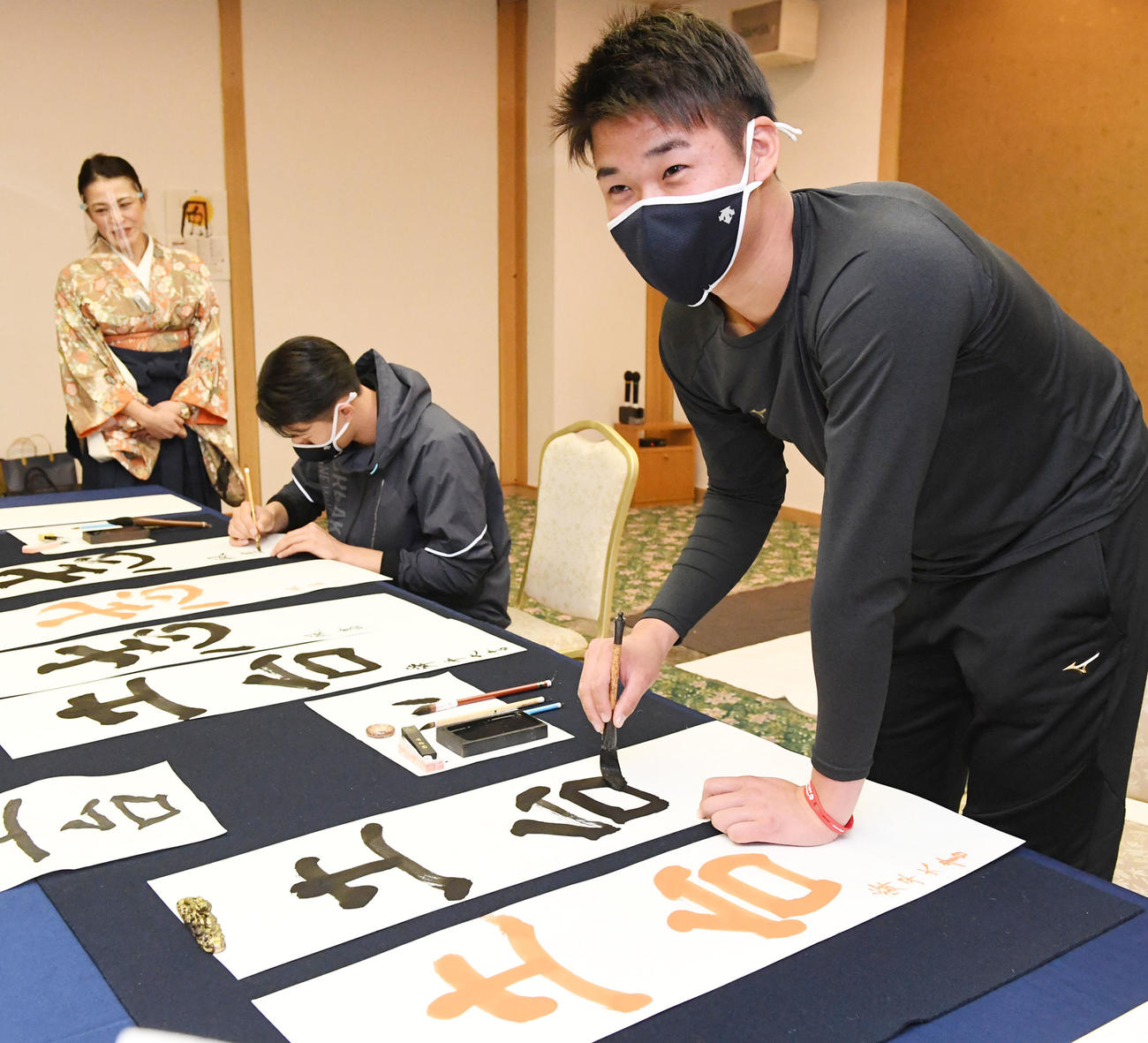 キャンプ休日に毛筆で今年の目標を記す山下（右）と中川颯は、本番を前に練習する。左端は今井美恵子講師（撮影・前岡正明）
