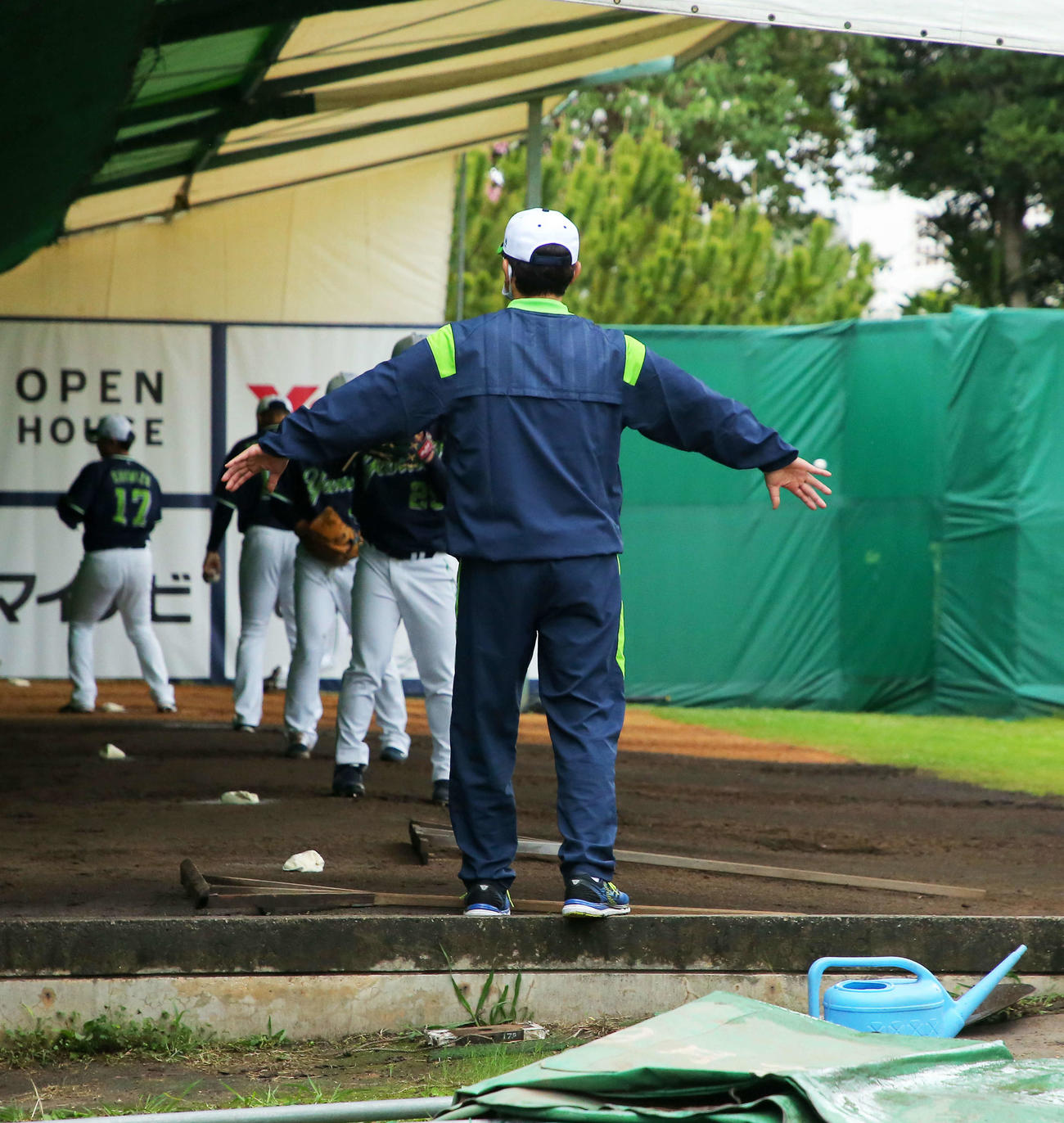 強風の影響でブルペンのパーテーションが倒れ、両手を広げ壁になる古田臨時コーチ（撮影・河田真司）
