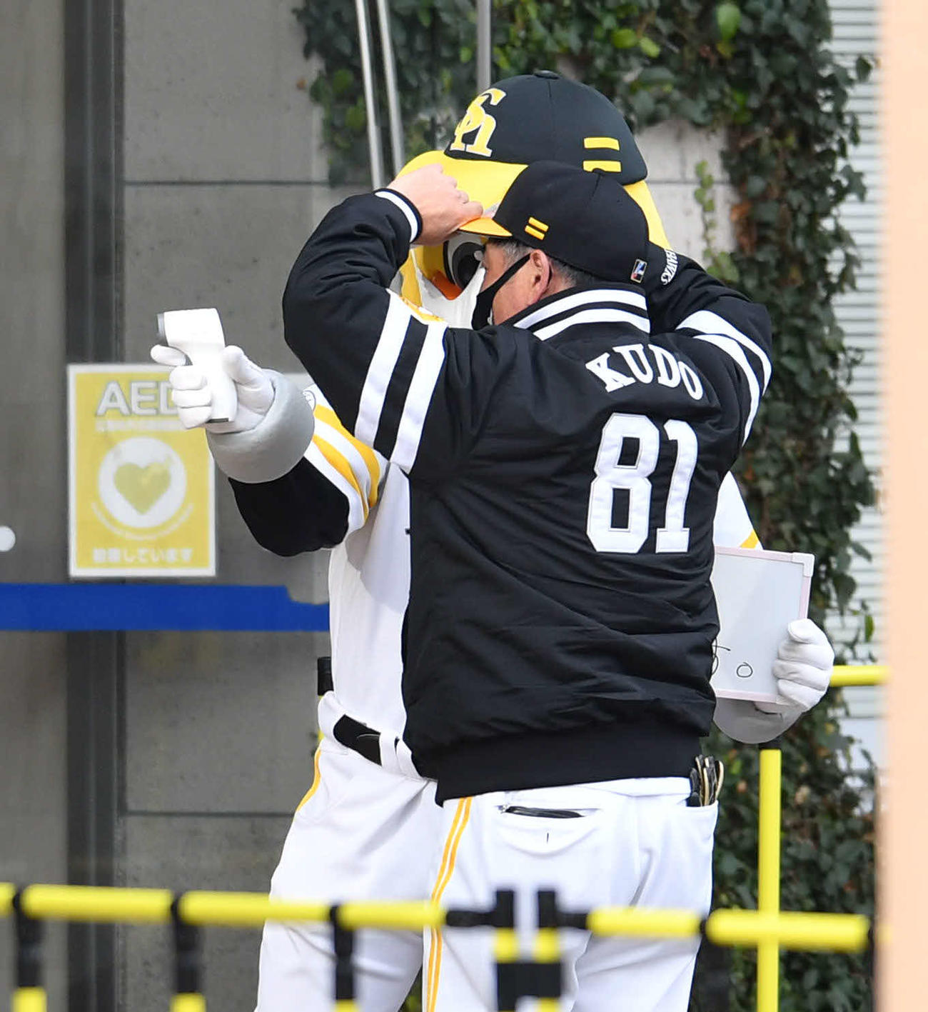 球場の入り口で工藤監督（右）を検温し、結果を見せるハリーホーク（撮影・岩下翔太）