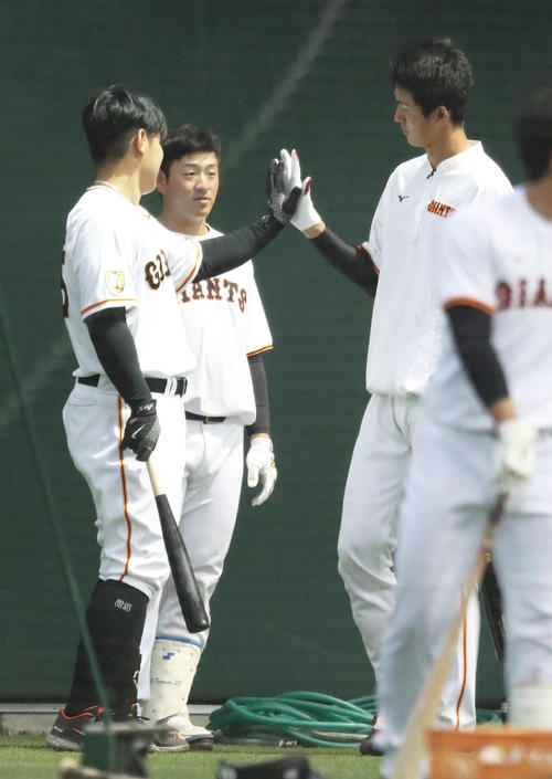 手のひらを合わせて大きさを比べる巨人岡本和（左）と秋広（右）。中央は岸田