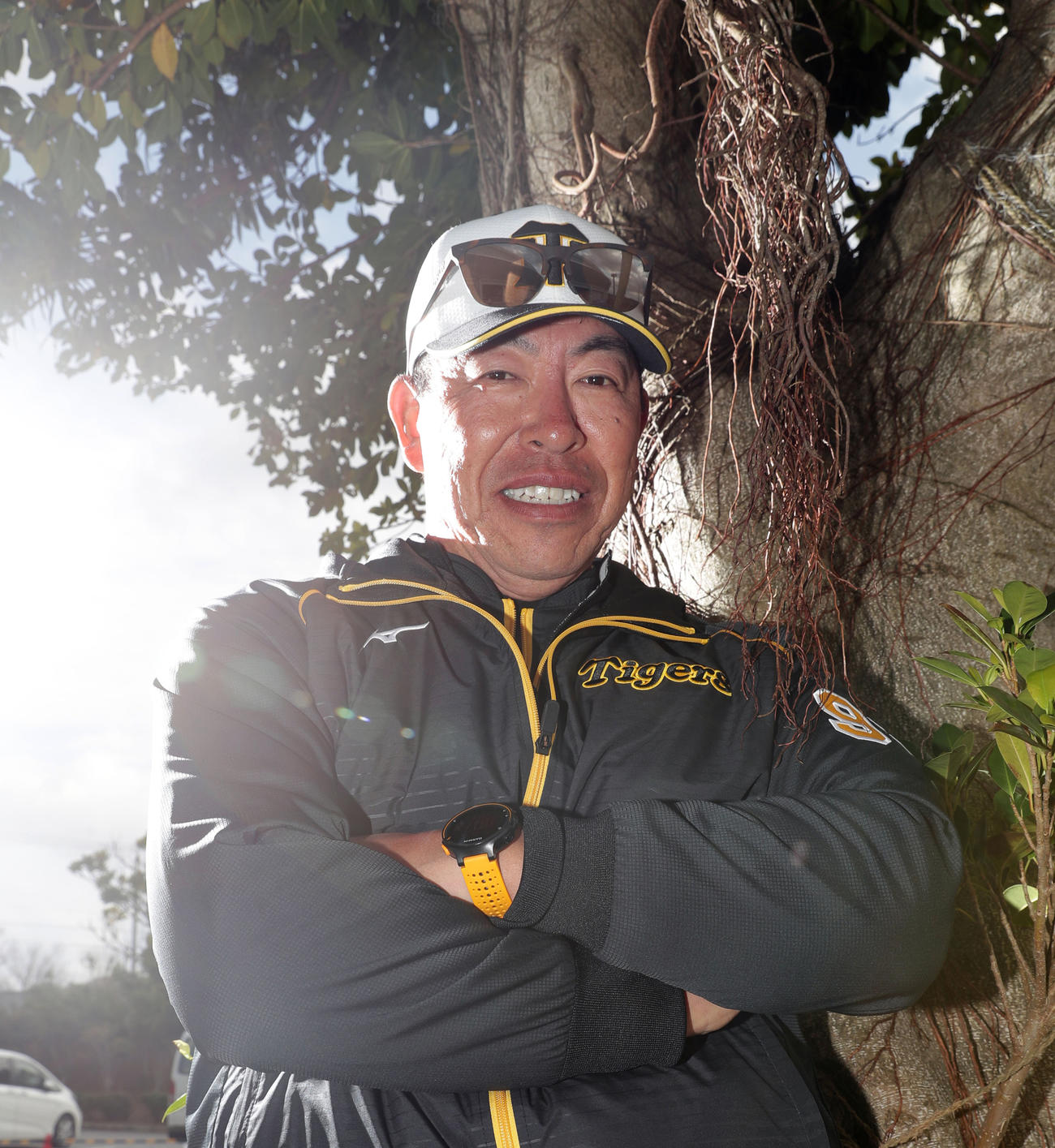 宜野座のガジュマルの木の前でポーズを決める阪神井上ヘッドコーチ（撮影・前田充）