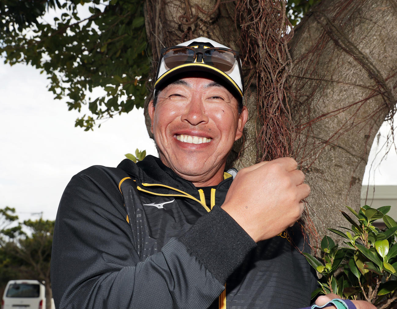 ガジュマルの木のツルで「髪の毛みたいだな！」と笑顔でおどける阪神井上ヘッドコーチ（撮影・前田充）