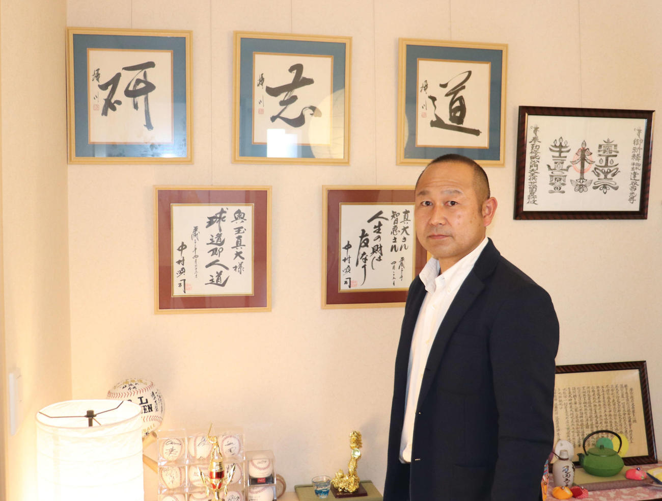 PL学園の恩師・中村順司元監督と同校先輩が書いた色紙の前に立つ奥玉監督（撮影・保坂淑子）