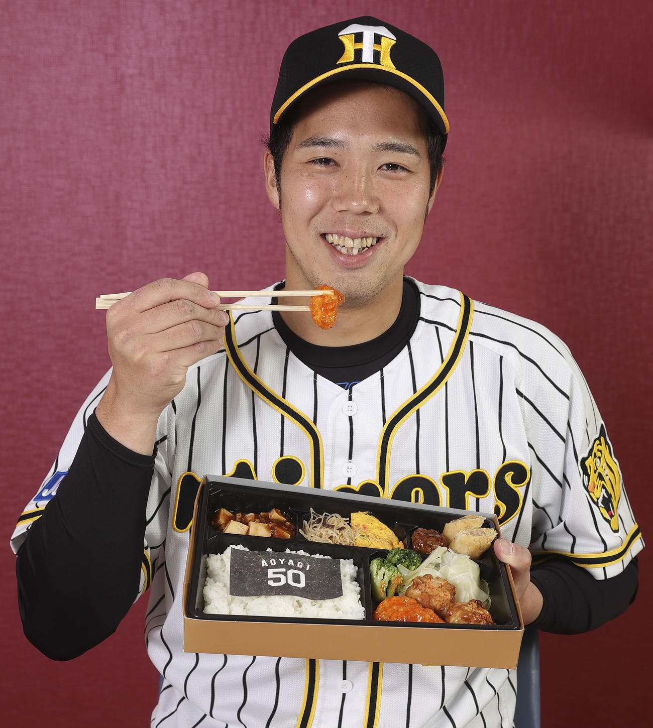 阪神矢野監督と選手22人がプロデュースするコラボグルメ　プロデュースしたグルメを持ち笑顔の青柳晃洋（阪神甲子園球場提供）