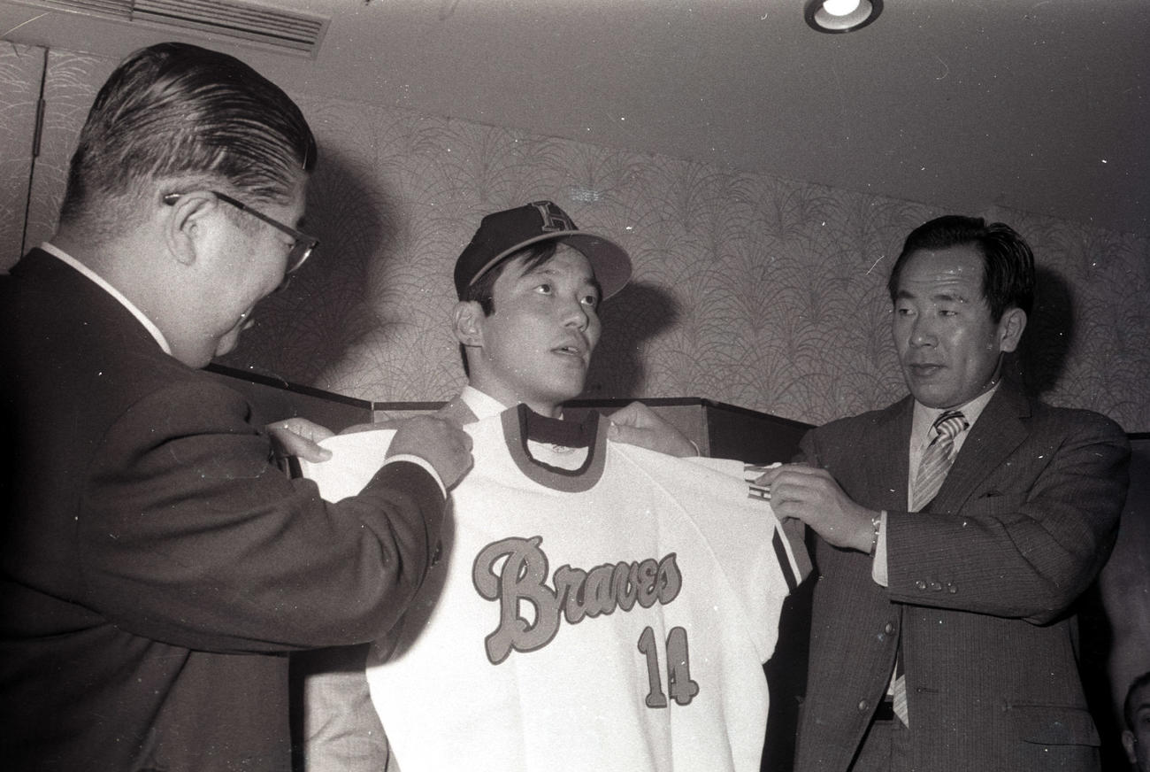 74年、阪急の入団会見で上田監督から14番のユニホームを重ねてもらう山口高志