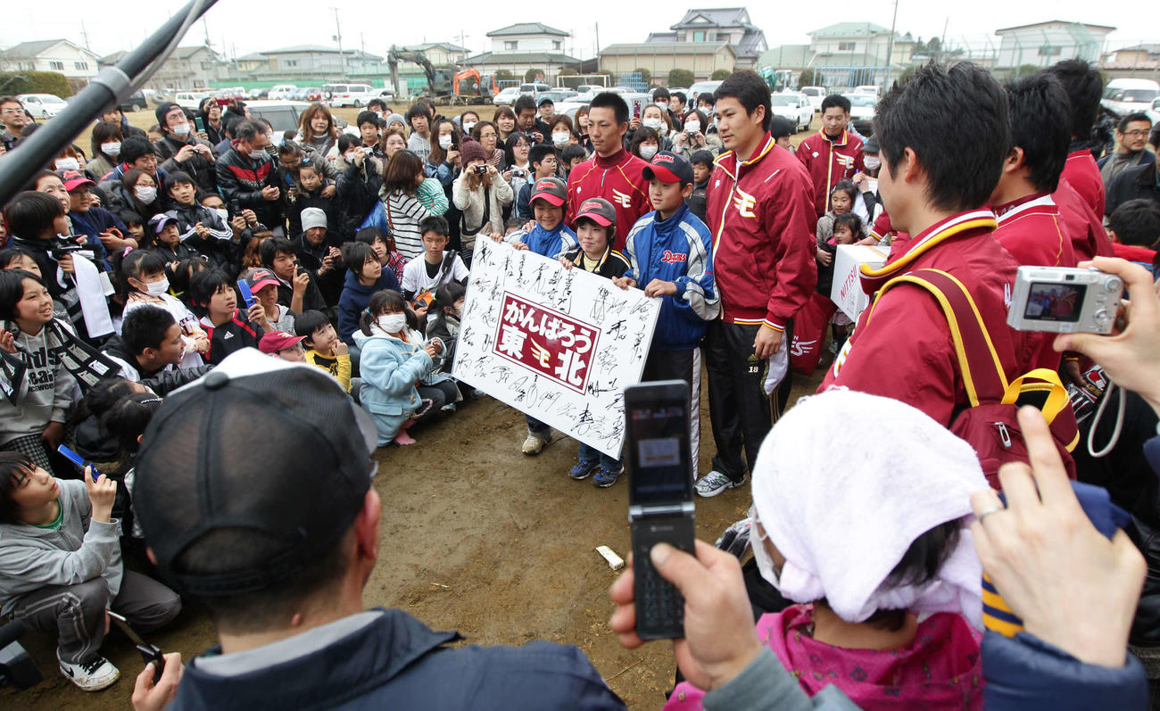 11年4月、宮城県東松島市立大曲小学校を訪れ大曲ドリームスの野球少年にメッセージボードを渡した嶋（左）と田中