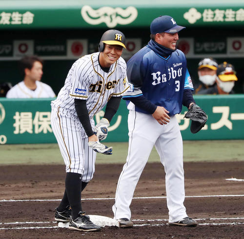 阪神対西武　2回裏阪神2死、佐藤輝は四球を選んで出塁し一塁手の山川から言葉を掛けられ笑顔を見せる（撮影・加藤哉）