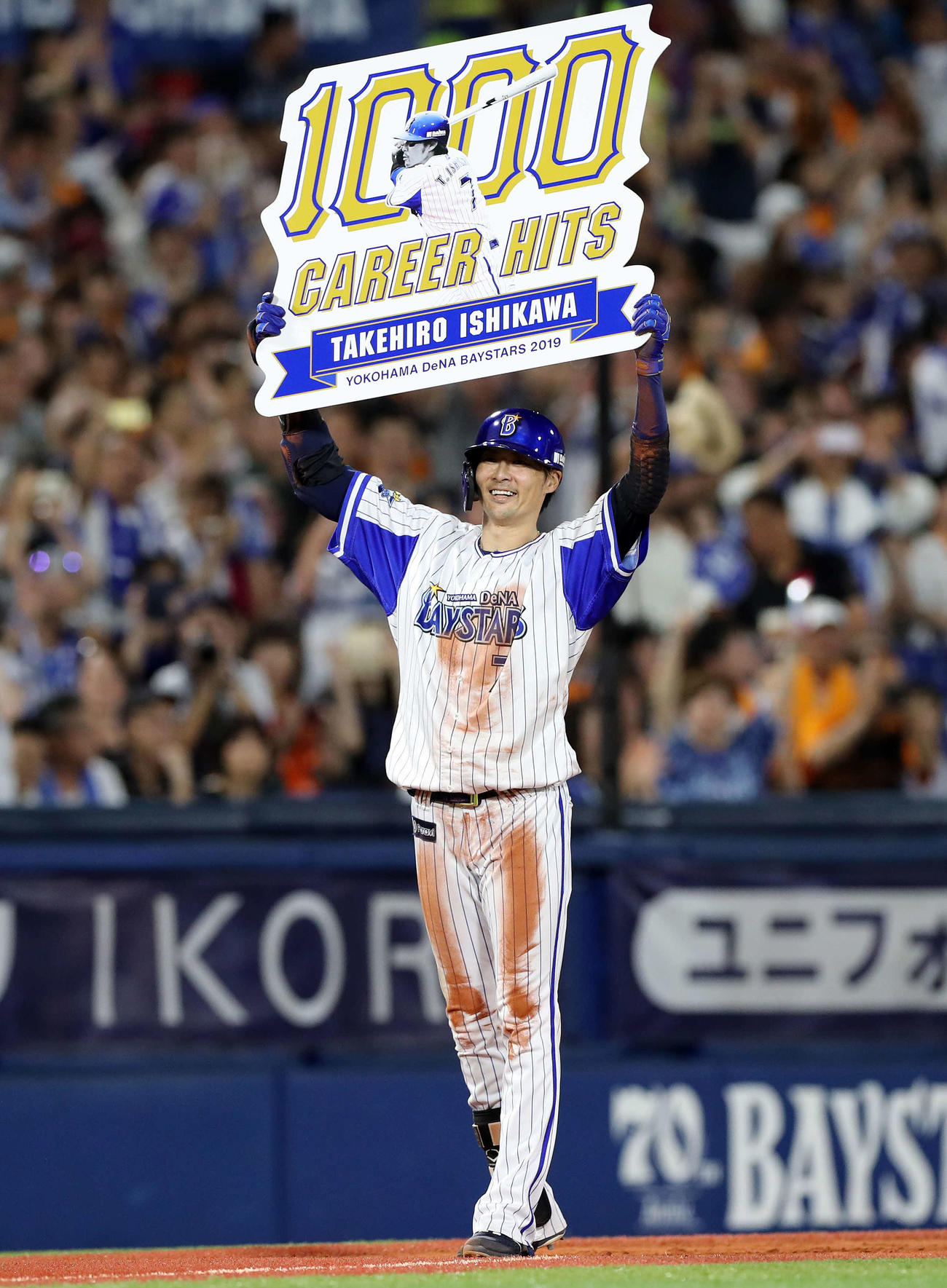 19年8月、巨人戦で石川雄洋は右越え三塁打を放ち通算1000安打のボードを上げ笑顔を見せる