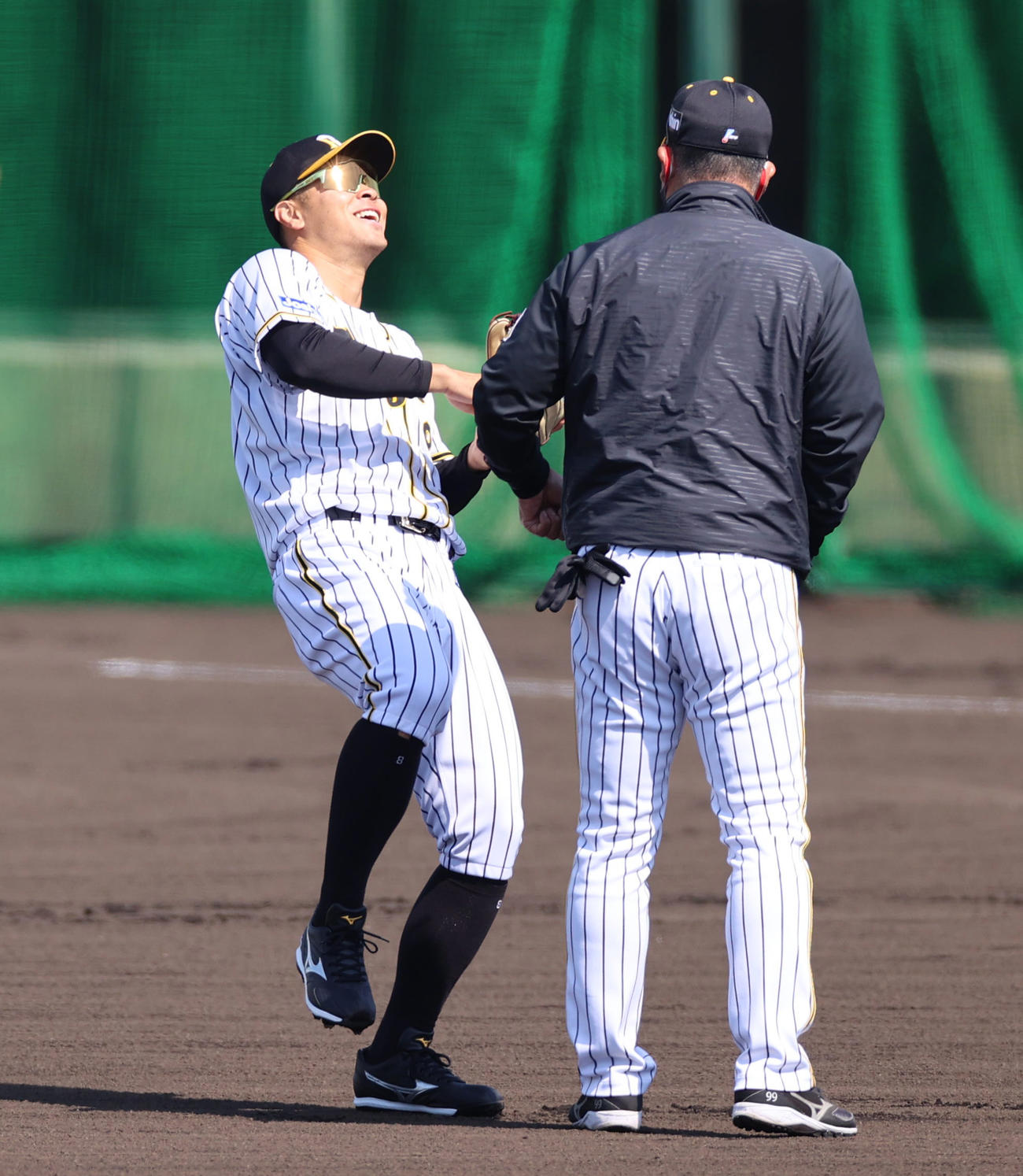 井上一樹ヘッドコーチ（右）からパンチを受け笑顔をみせる佐藤輝明（撮影・清水貴仁）