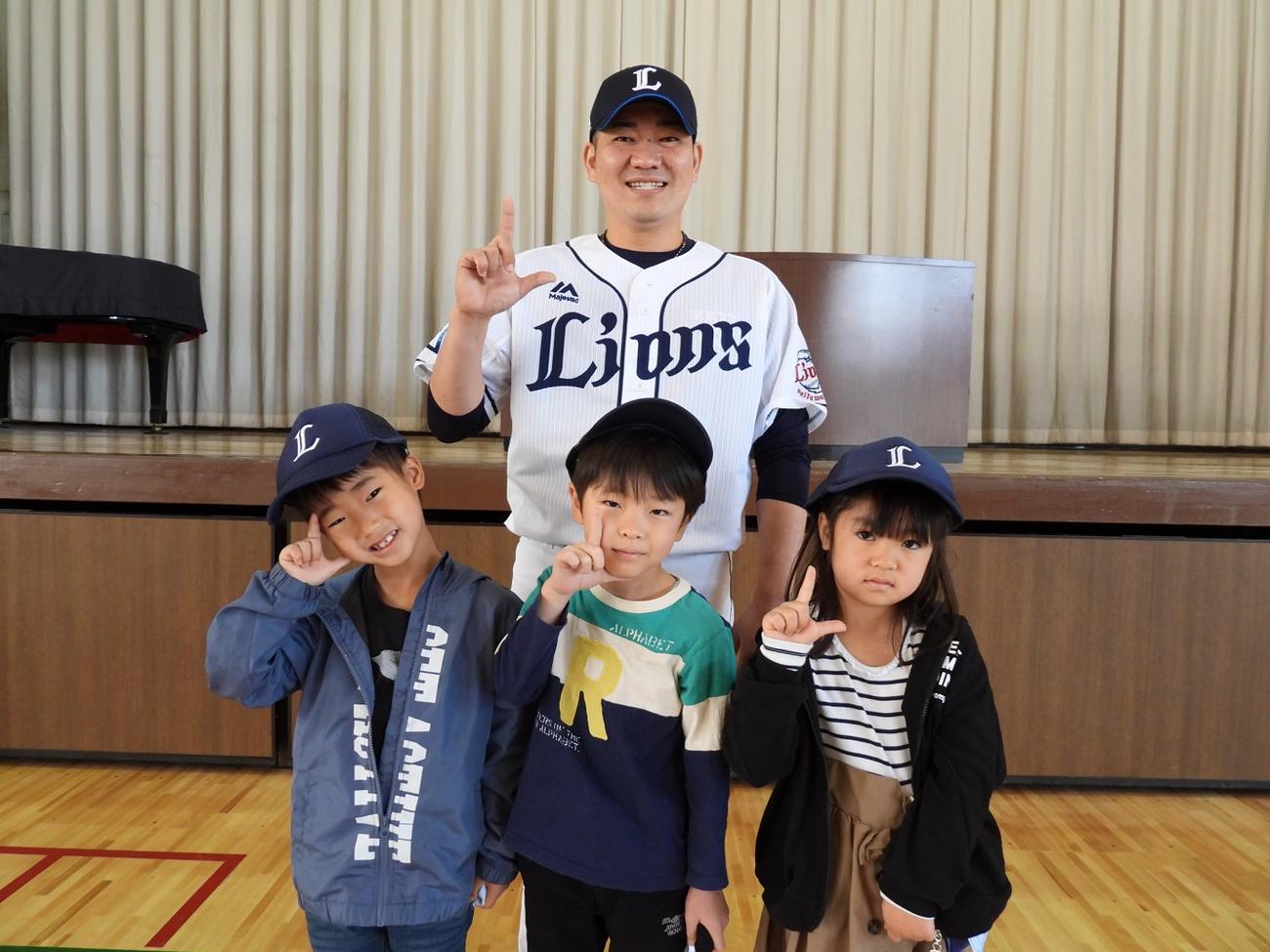 西武ライオンズアカデミーの高橋コーチは小学1年生に「ライオンズオリジナル・ベースボールキャップ」を手渡し、笑顔で記念撮影に納まる（球団提供）