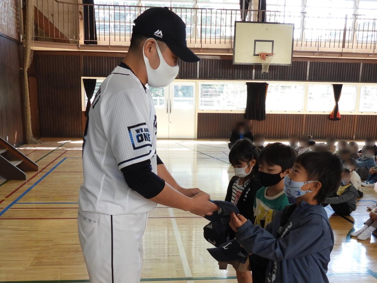 西武ライオンズアカデミーの高橋コーチが小学1年生に「ライオンズオリジナル・ベースボールキャップ」を手渡した（球団提供）