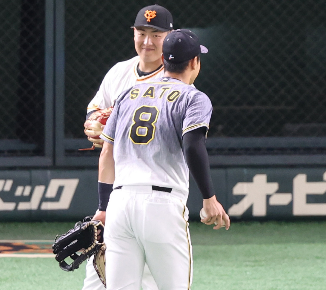 巨人対阪神　試合前、佐藤輝（手前）からあいさつされ、笑顔で応える岡本和（撮影・狩俣裕三）