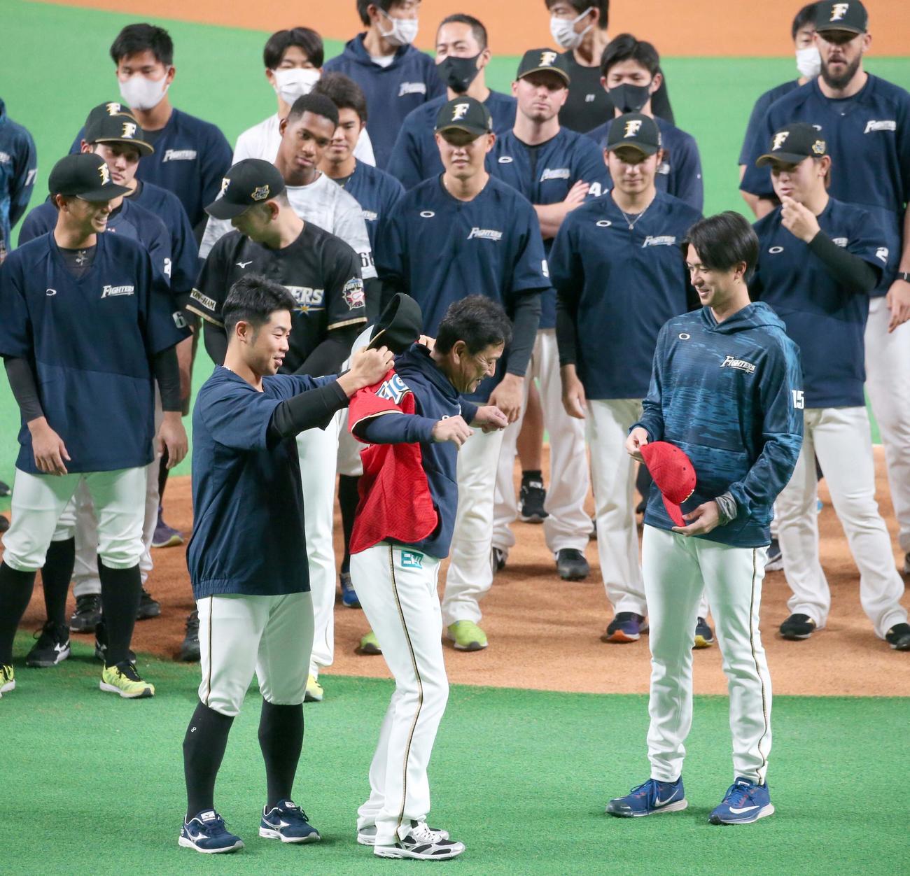 近藤に還暦祝いの赤いユニホームを着せてもらう栗山監督（撮影・黒川智章）