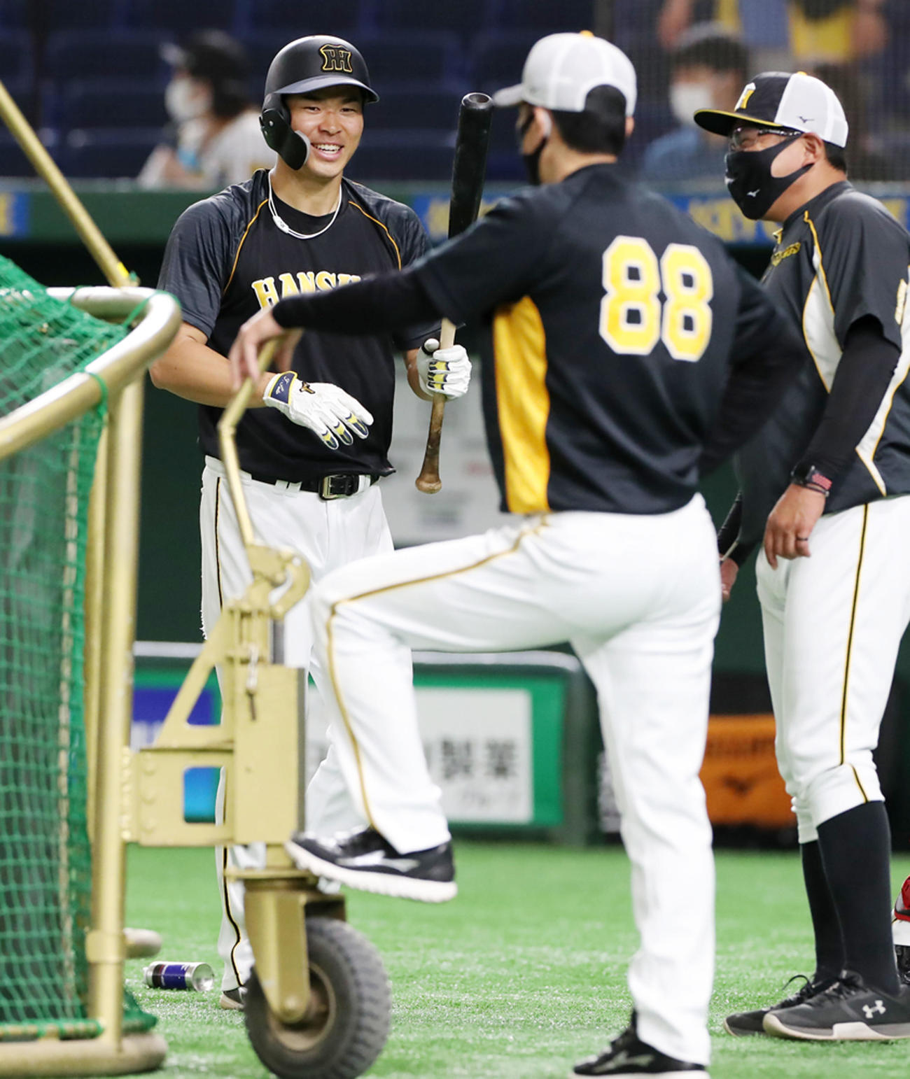 巨人対阪神　打撃練習中、ケージの後方で笑顔を見せる佐藤輝。右は矢野監督。右端は北川コーチ（撮影・加藤哉）