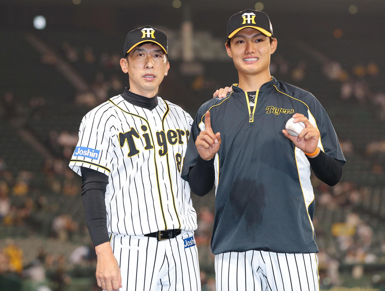 プロ初勝利を挙げ、勝利球を手に笑顔でポーズを決める阪神西純。左は祝福する矢野監督（2021年5月19日撮影）