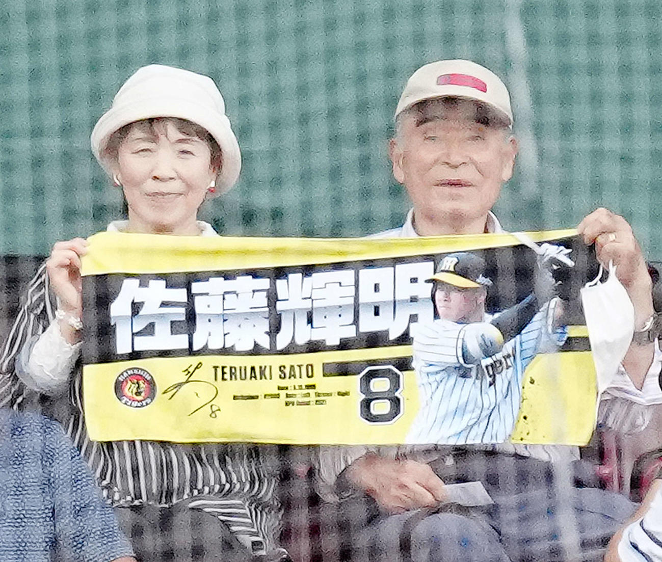 楽天対阪神　試合前、客席で取材に応じ、阪神佐藤輝のタオルを広げ写真に納まる祖父・勲さん（右）と祖母・美智恵さん（撮影・江口和貴）