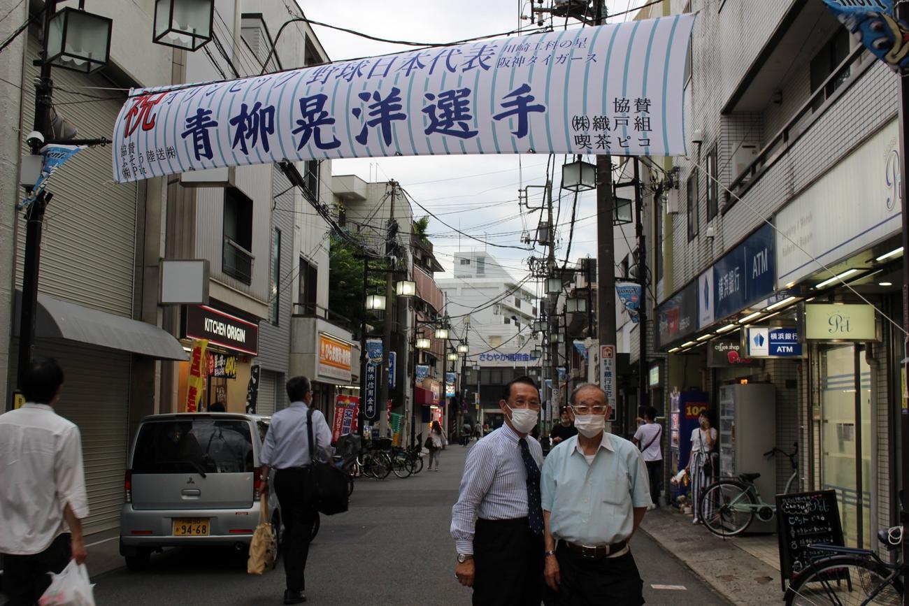 阪神青柳の横断幕制作の発起人である南武線平間駅近くのジュエリー店、Pitの三浦尚敏社長。右は協賛の喫茶ピコの店主清水和夫さん（本人提供）