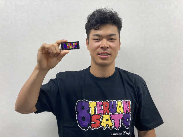 阪神佐藤輝は自らプロデュースしたTシャツを着てアクリルキーホルダーを手に持つ（球団公式ツイッターより）
