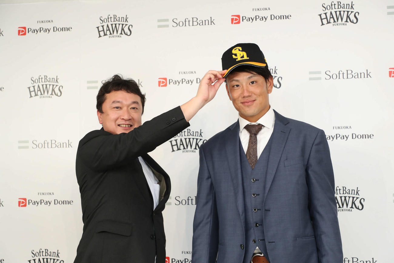 入団会見で三笠杉彦取締役GM（左）から帽子を被せてもらい笑顔を見せる中谷将大（球団提供）