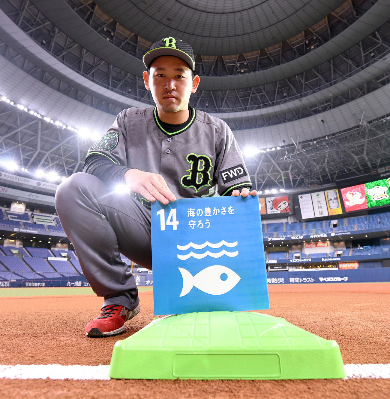 SDGs活動の象徴として使用するグリーンのベースを指さすオリックス宮城（球団提供）