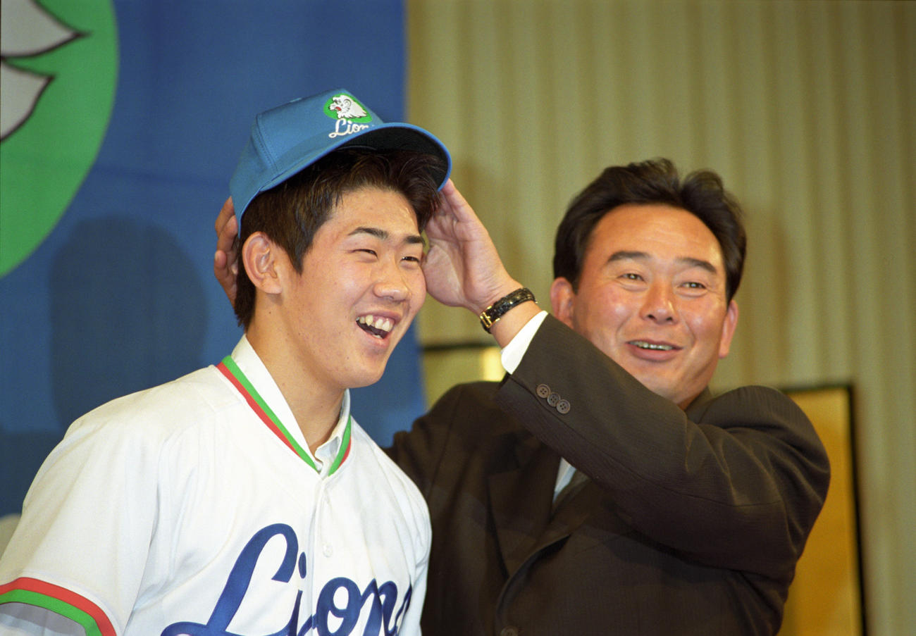 98年12月、西武入団会見で東尾修監督に帽子をかぶせてもらい笑顔を見せる松坂
