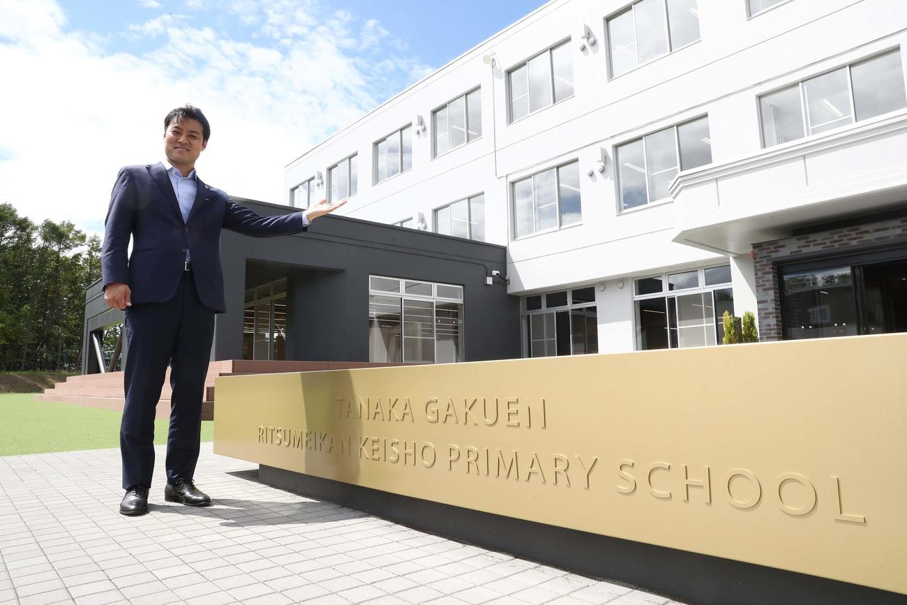 田中学園立命館慶祥小学校前でポーズをとる田中理事長（撮影・黒川智章）