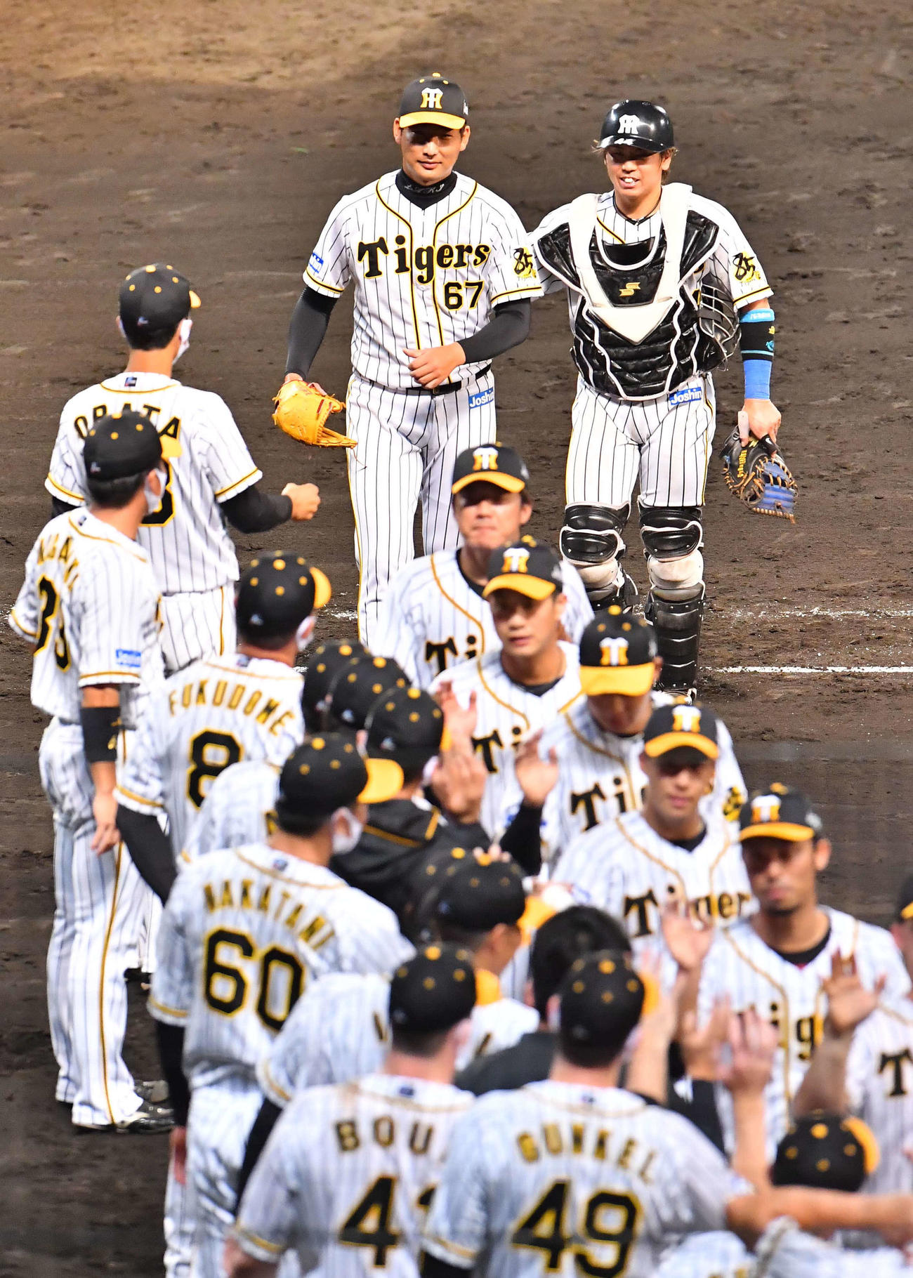 2020年9月3日　阪神対ヤクルト　初セーブをあげ梅野（右奥）と笑顔を見せる岩崎