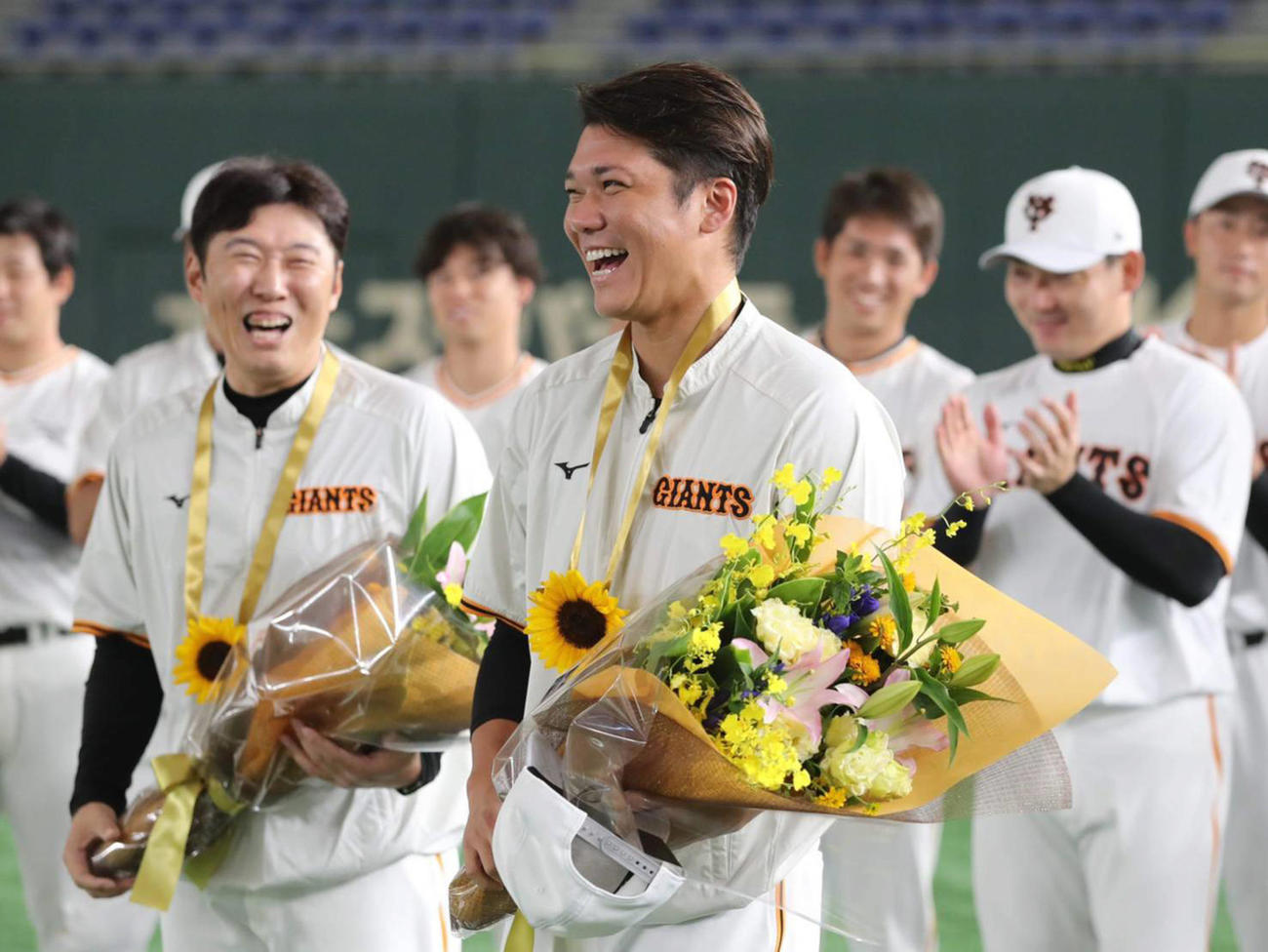 練習前、ひまわりのメダルと花束をチームメートから贈呈され、笑顔を見せる坂本（右）。左は村田ブルペンコーチ（球団提供）
