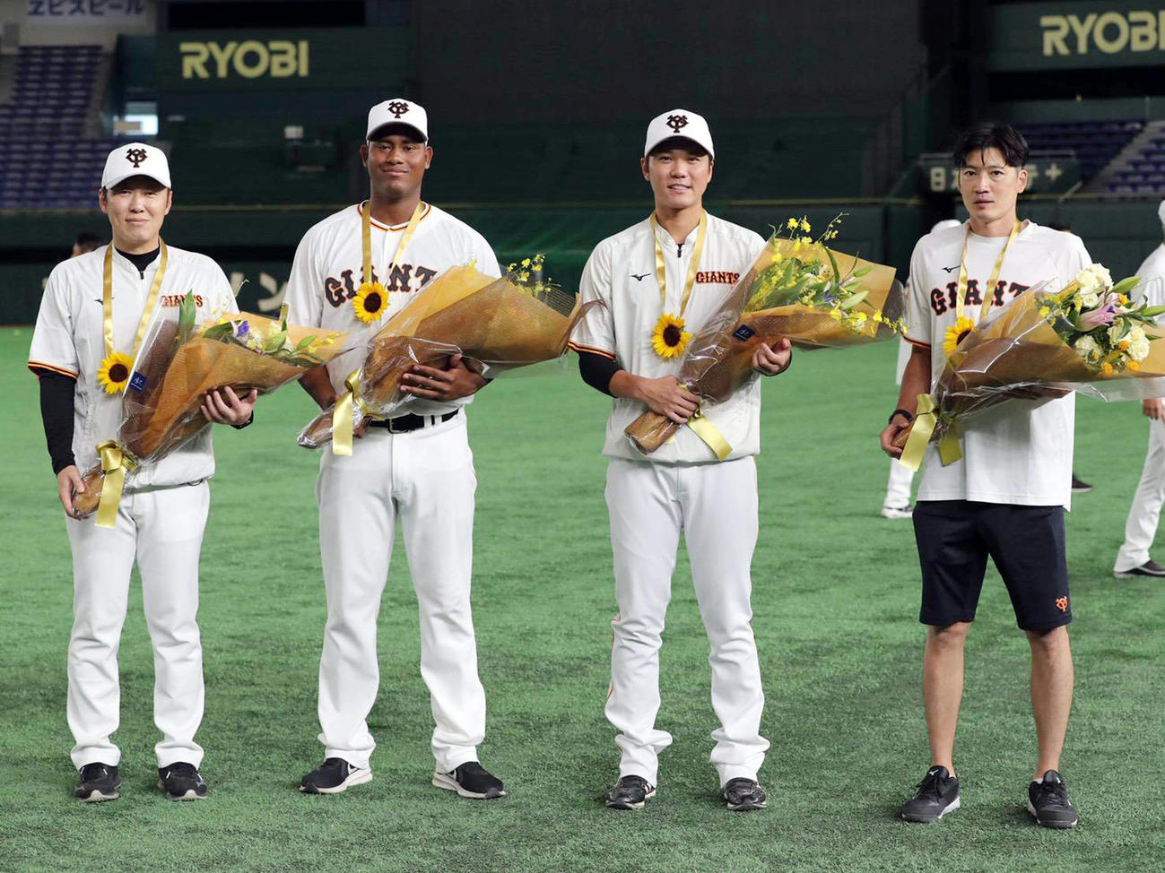 練習前、ひまわりのメダルと花束をチームメートから贈呈され、記念撮影する、左から村田ブルペンコーチ、メルセデス、坂本、根津トレーナー（球団提供）