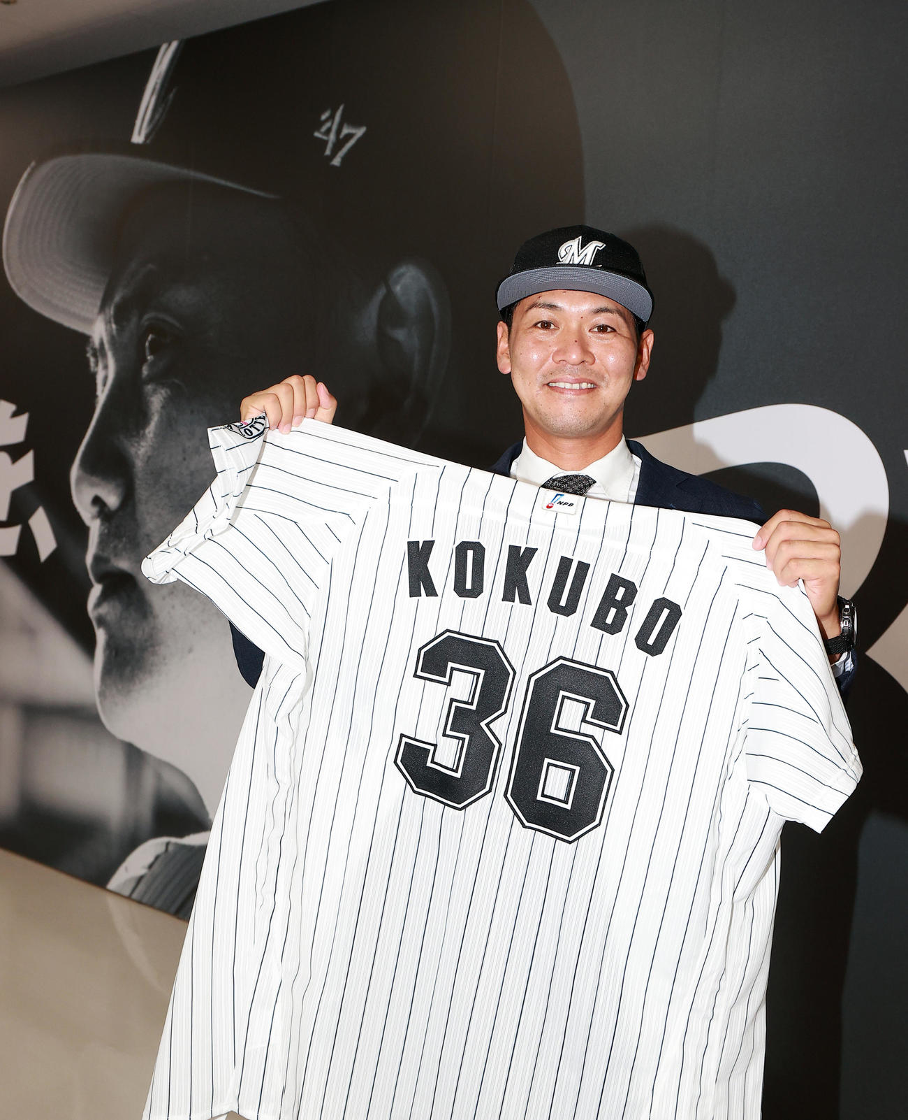 ロッテ入団会見に臨んだ小窪は、井口監督の写真を背に、背番号36のユニホームを持って笑顔を見せる（撮影・浅見桂子）
