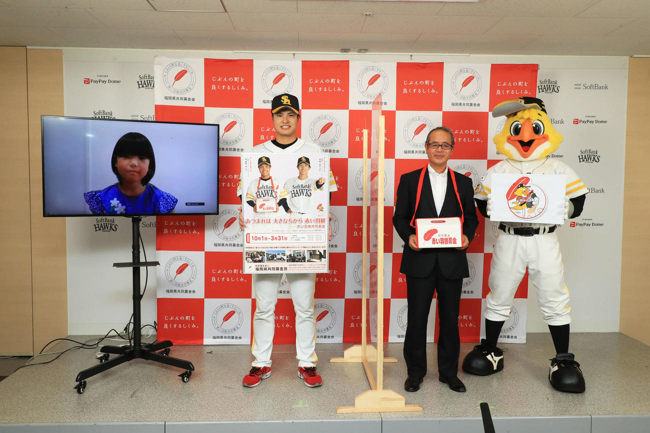 「第75回赤い羽根共同募金運動」の応援大使を拝命した甲斐野。右は福岡県共同募金会常務理事塩川正一氏。モニター内は募金運動キャッチフレーズ考案者の古野結月さん（球団提供）