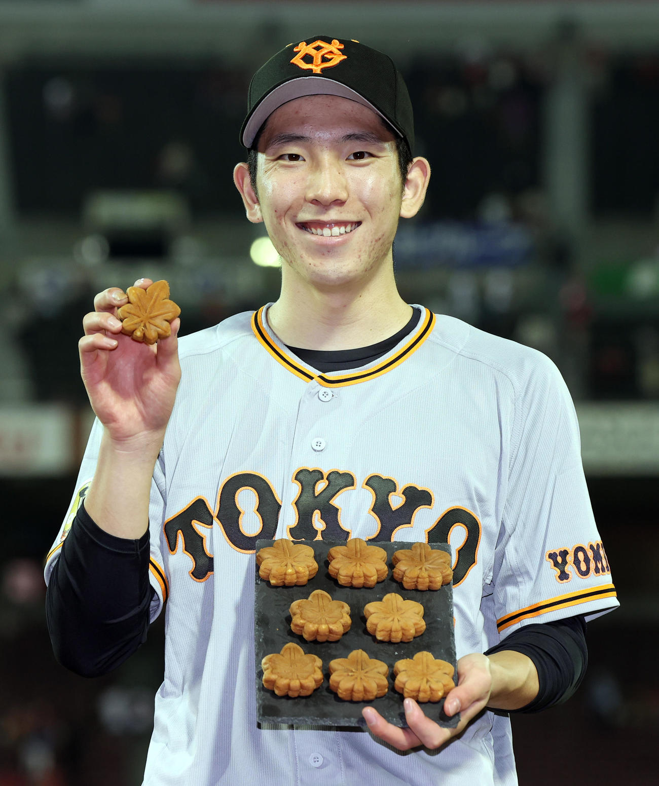 広島対巨人　9勝目を挙げ、9個のもみじまんじゅうを手に笑顔を見せる戸郷（撮影・狩俣裕三）