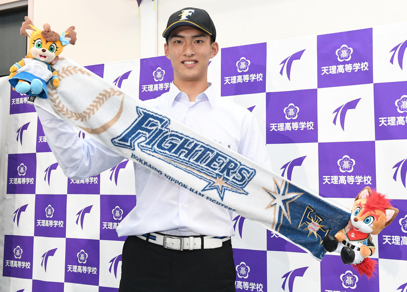 日本ハムから1位に指名された天理・達は、球団グッズを手に笑顔を見せる（撮影・滝沢美穂子）