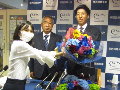 巨人に1位指名され、職員から祝福の花束を受け取関西国際大・翁田大勢投手（右）、中央は鈴木英之監督＝撮影・高垣誠