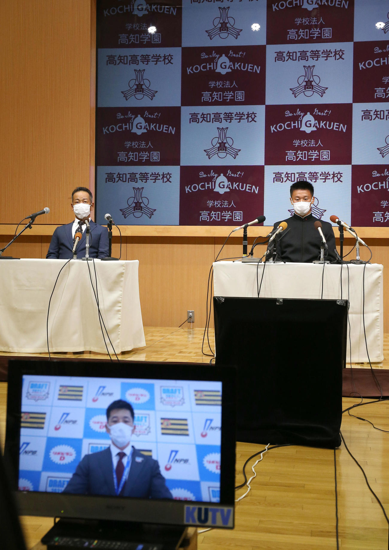 ドラフト会議中にモニターで映し出される阪神の矢野監督をテレビで見る高知の森木。左は高知の浜口監督（撮影・上山淳一）