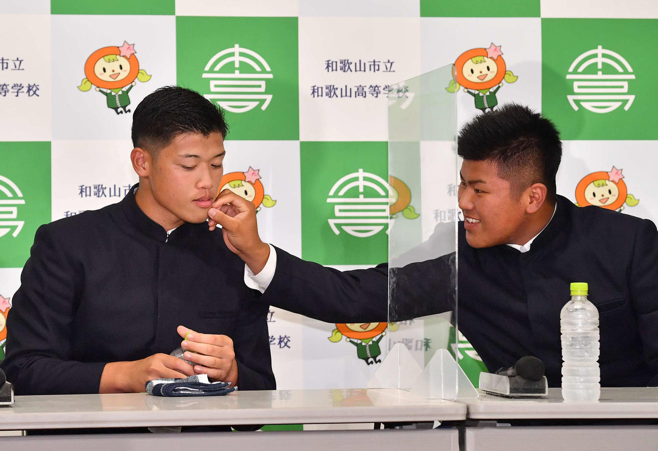 DeNAに1位指名された市和歌山・小園（左）は、口元についたマスクの繊維をロッテ1位指名の松川に取ってもらう（撮影・上田博志）